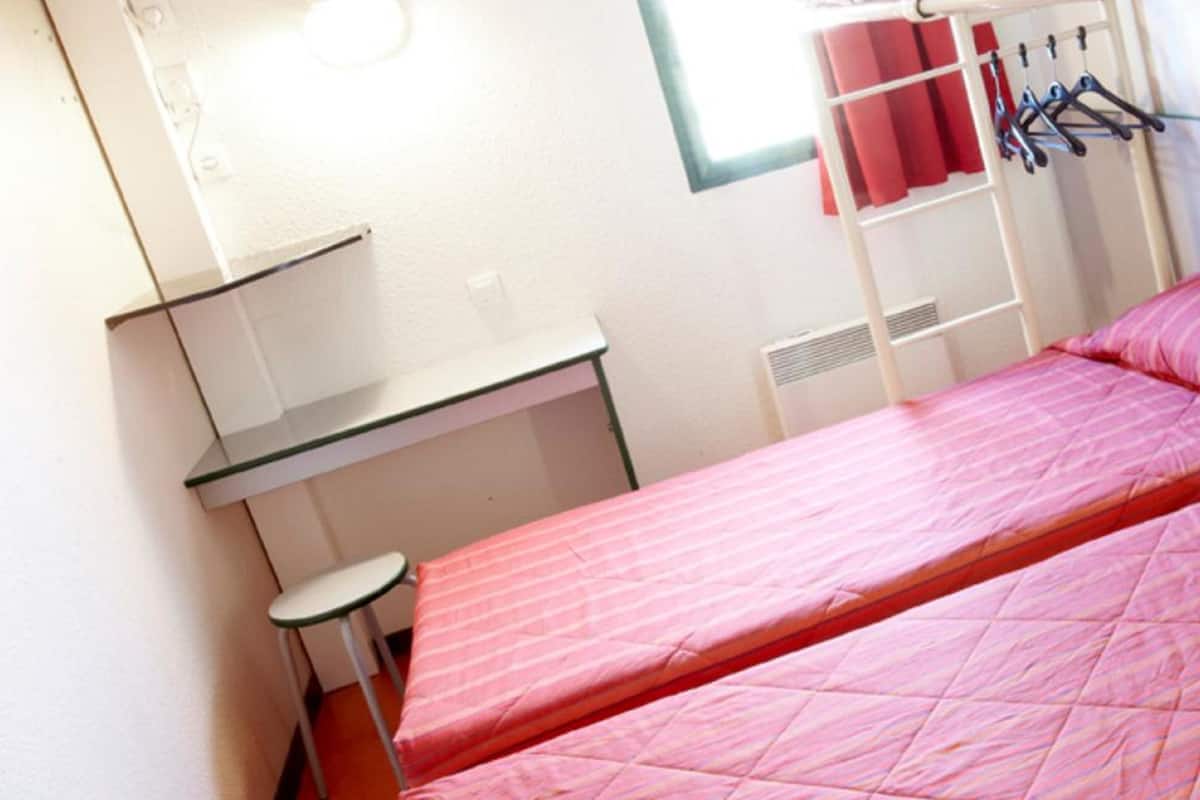 Une petite pièce avec deux lits, un bureau et une chaise.