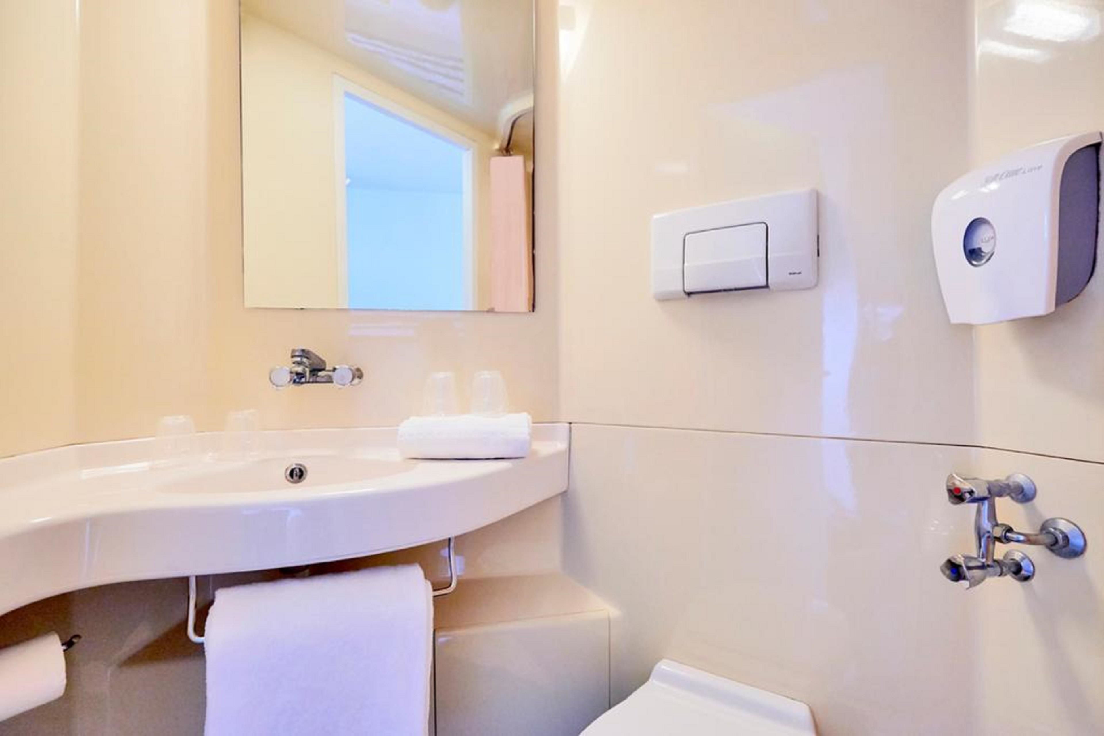 Une salle de bain moderne avec un grand lavabo, un miroir, un porte-serviettes, un distributeur de savon et des toilettes.