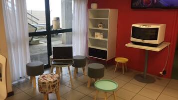 Una habitación con televisión sobre un mueble bajo, una mesita, una silla y una estantería.