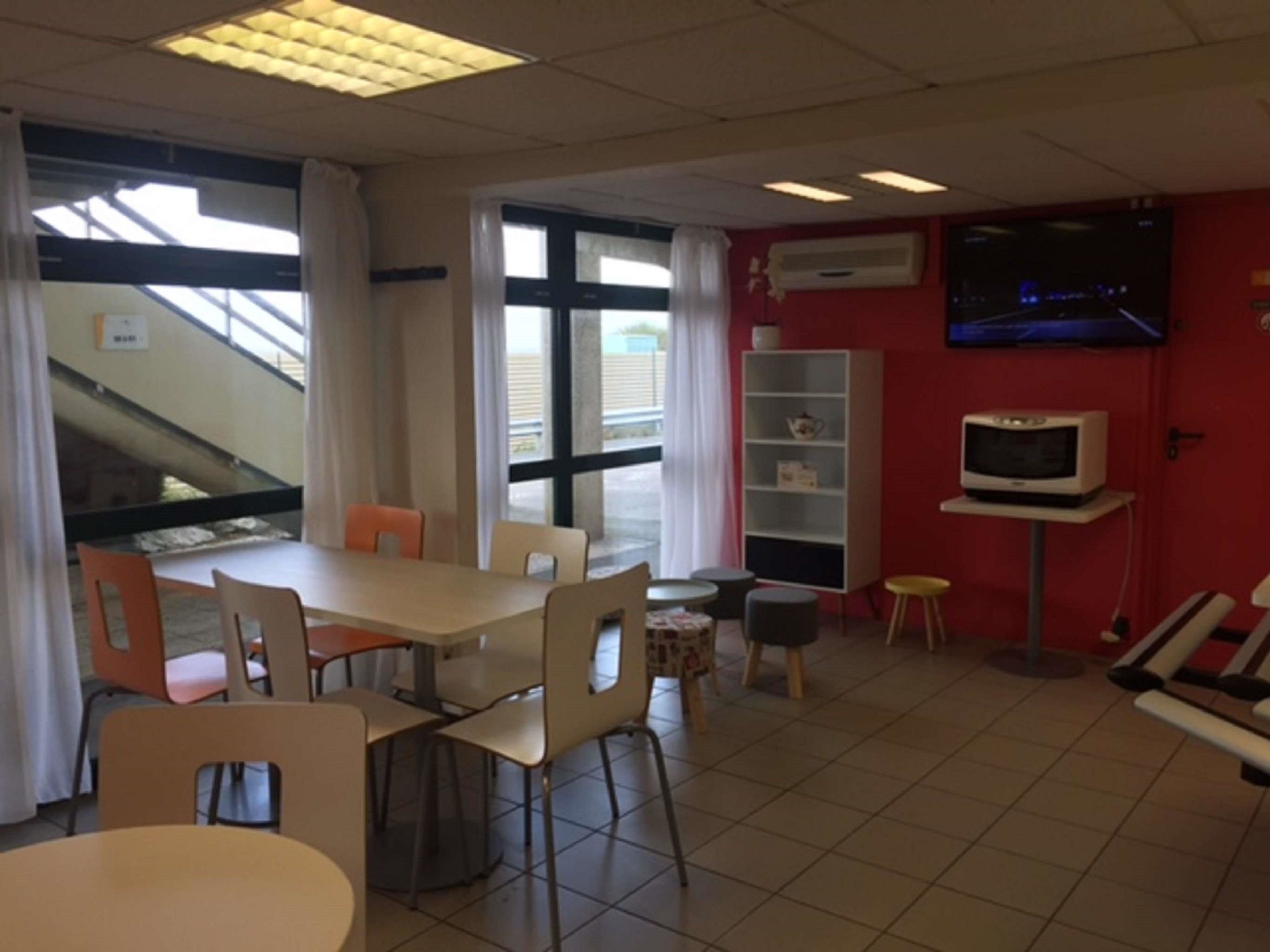 Un coin repas avec une table et des chaises, une petite télévision posée sur un meuble, et une bibliothèque.
