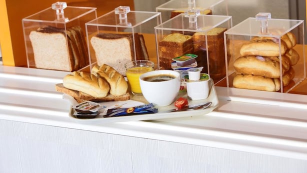 A breakfast display with various breads, pastries, and condiments in clear containers.