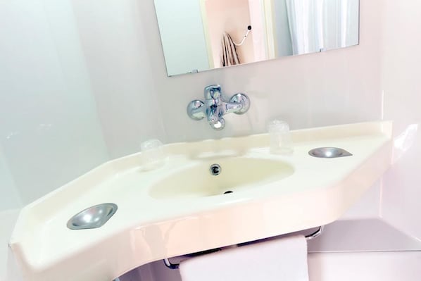 Un baño con un lavamanos blanco, un espejo encima y una toalla colgada en un perchero.
