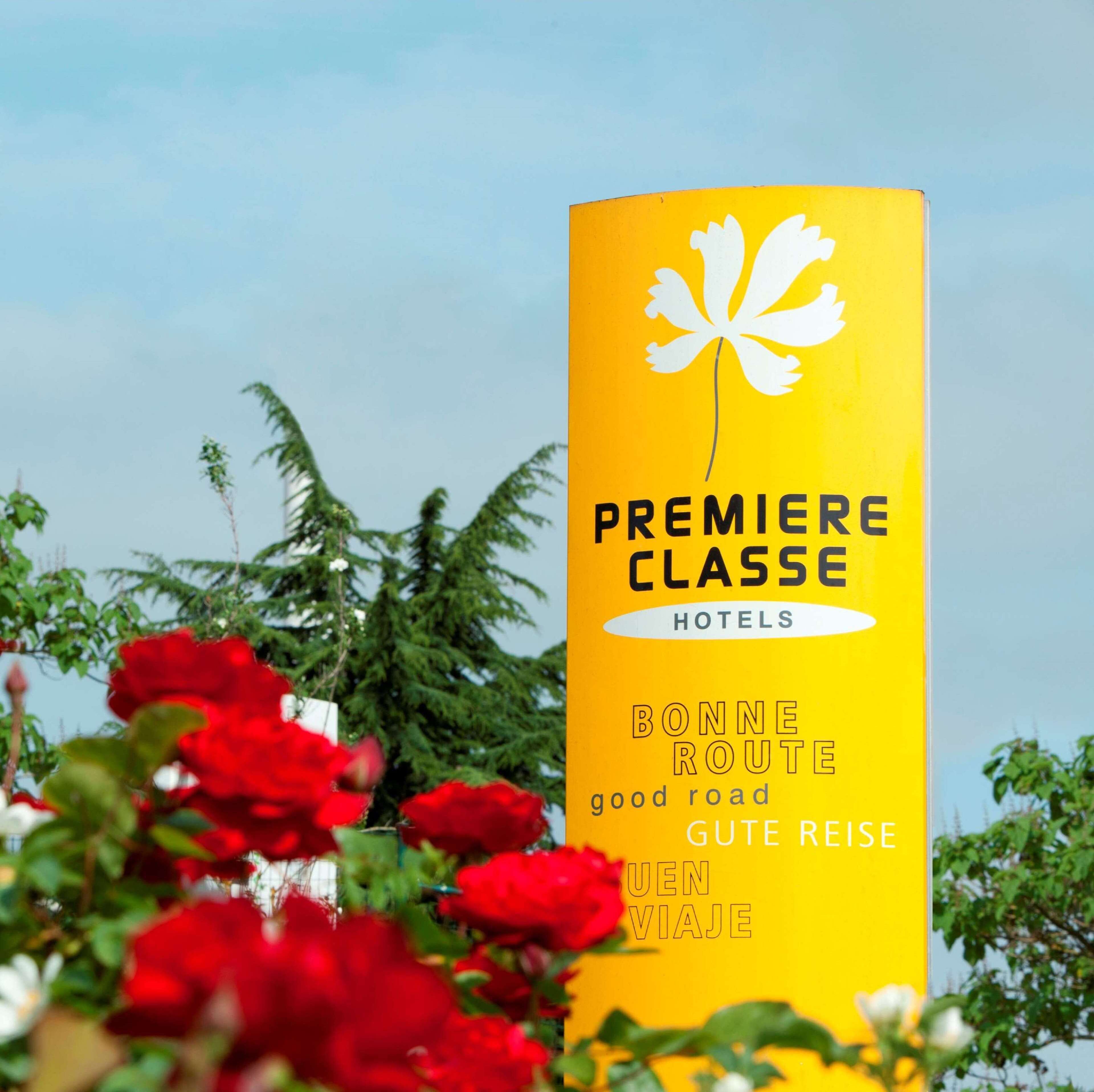 A yellow sign for Premiere Classe Hotels with a white flower symbol, surrounded by red flowers.
