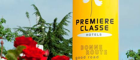 A yellow sign for Premiere Classe Hotels with a white flower symbol, surrounded by red flowers.