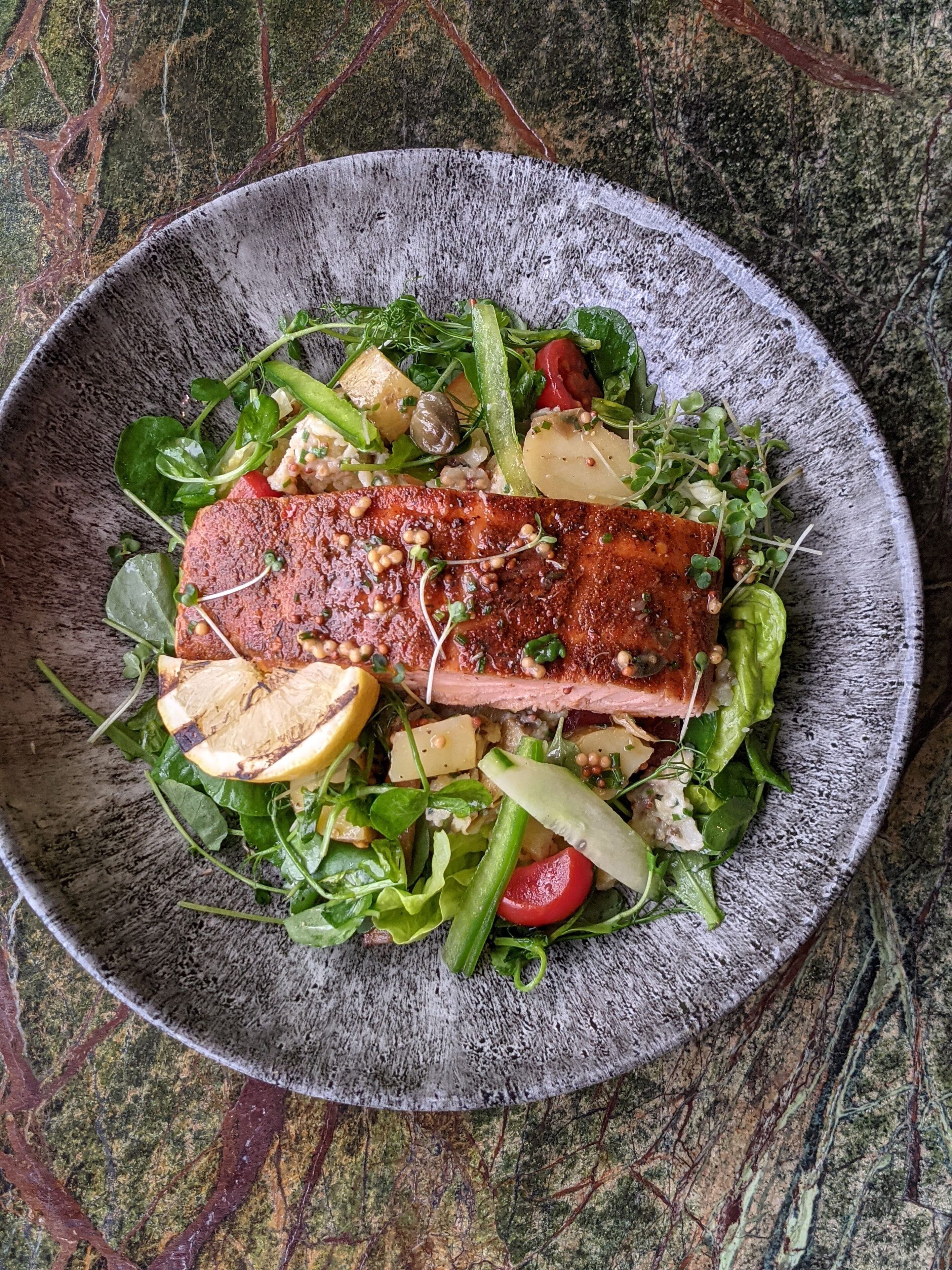 A bowl of food with a piece of salmon, greens, and potatoes.