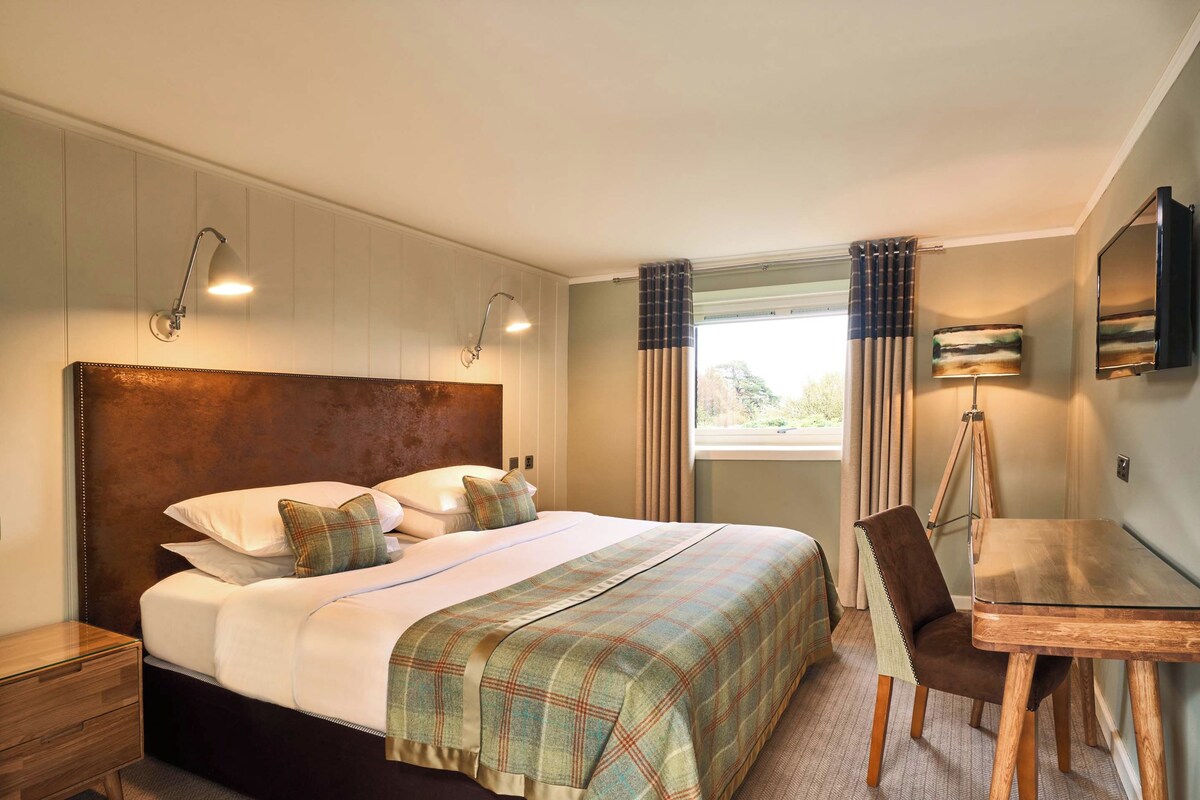 A hotel room with a large bed, a desk, and a chair.