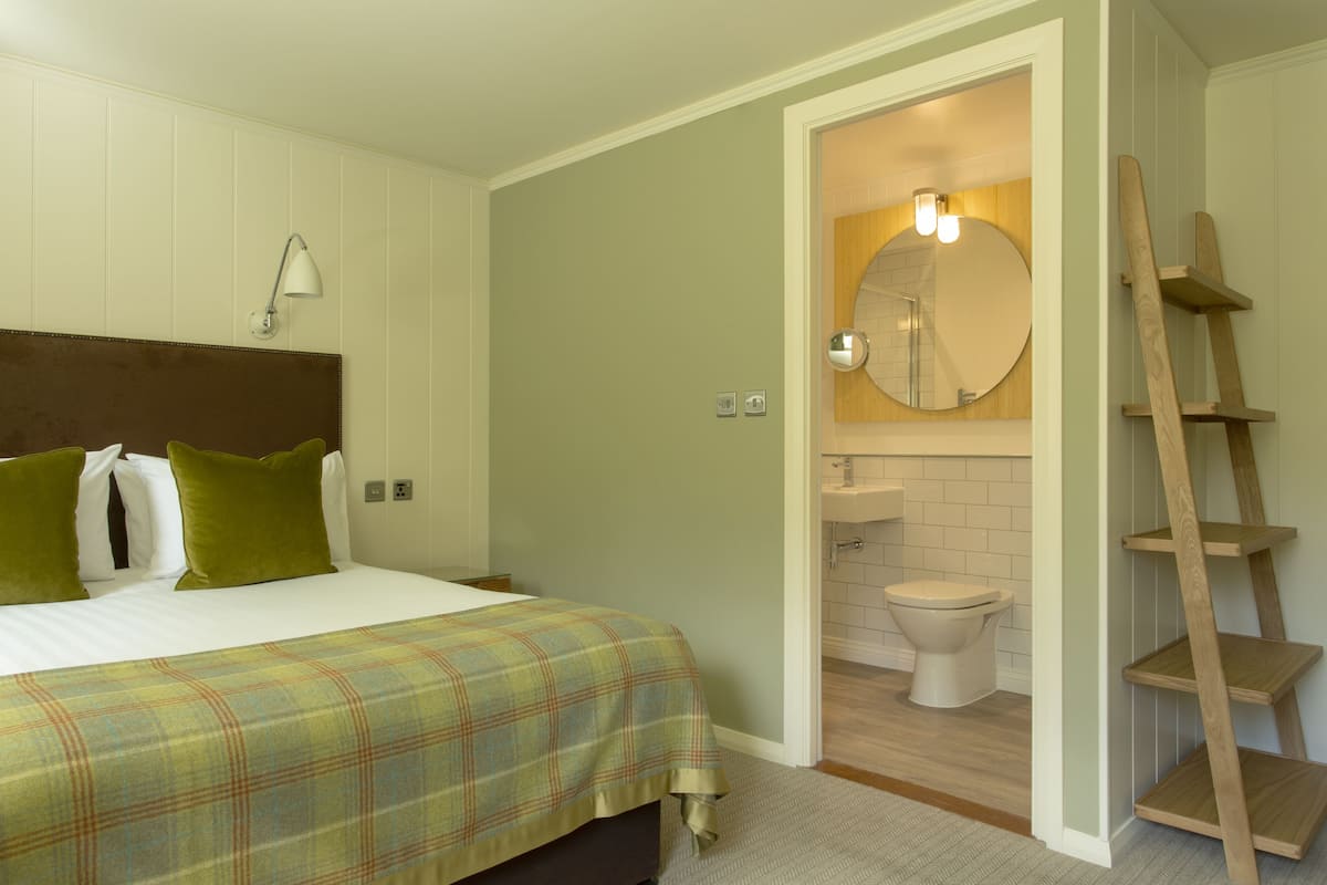 A bedroom with a bed, pillows, a bedside lamp, and a wooden ladder in the bathroom.