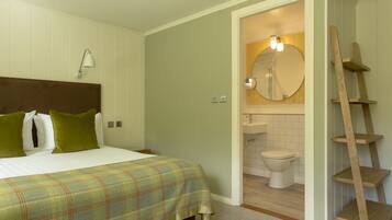 Een slaapkamer met een bed, kussens, een bedlampje en een houten ladder in de badkamer.