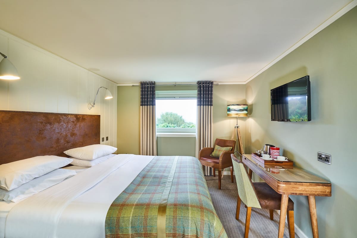 A hotel room with a bed, a desk, a chair, a television, and a window with curtains.