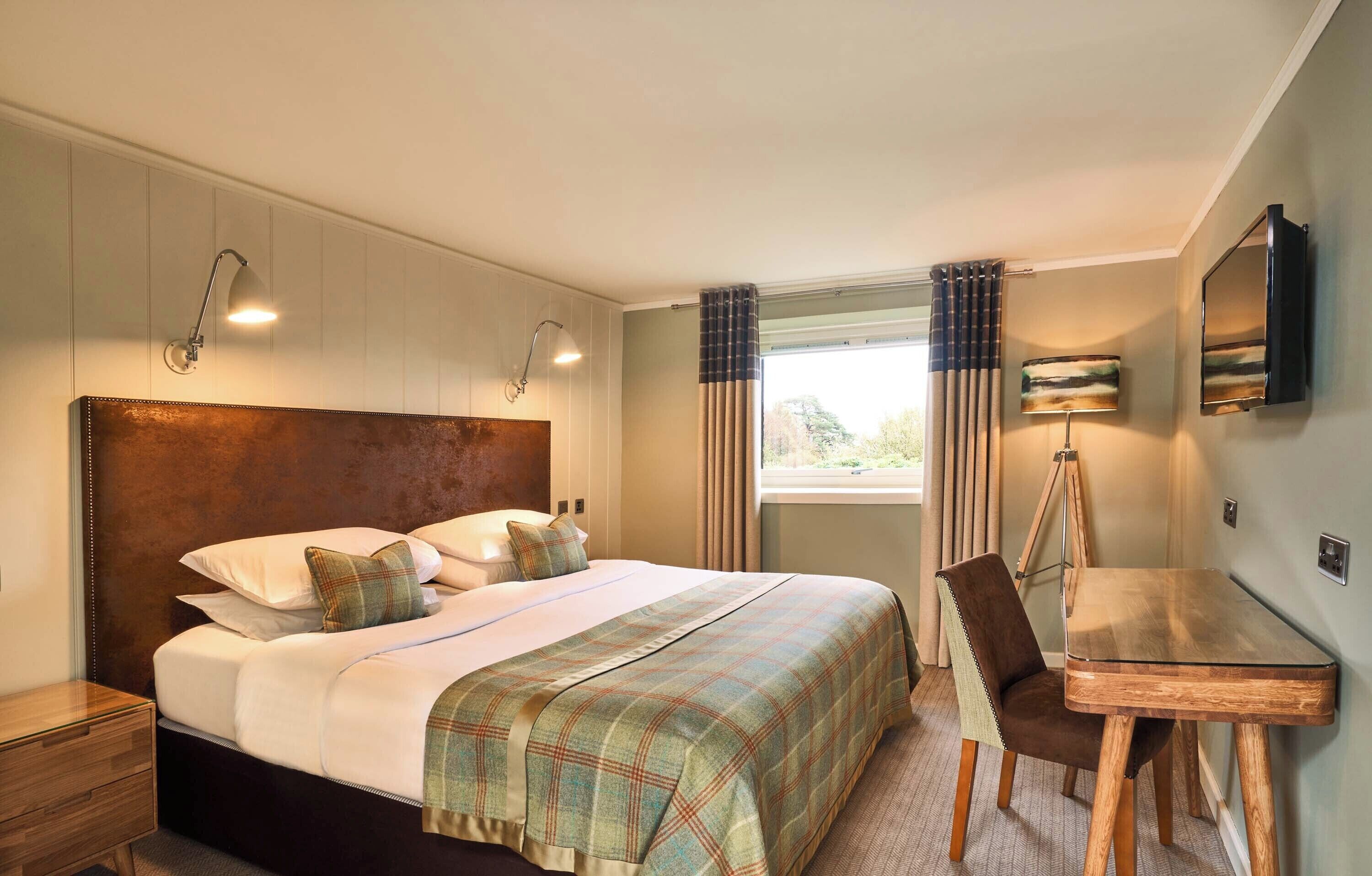 Une chambre d’hôtel avec un grand lit, un bureau, une chaise, une télévision et une fenêtre avec des rideaux.
