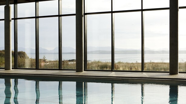 A swimming pool with clear water, large windows, and a view of a natural landscape with mountains and vegetation. - The Isle of Mull Hotel and Spa (Isle of Mull)