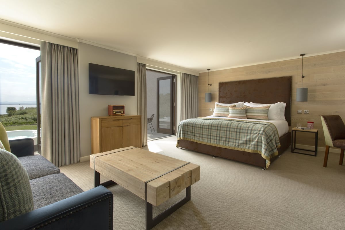 A hotel room with a bed, a TV, a wooden table, a sofa, and a view of the outdoors.