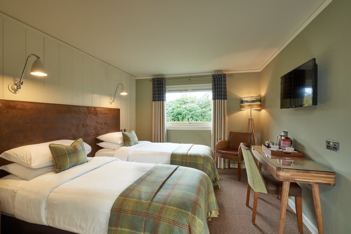 A hotel room with two beds, a desk, a chair, a television, and a window with curtains.