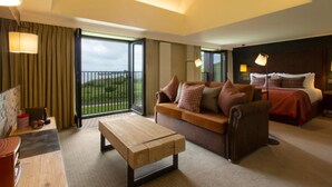 A hotel room with a sofa, a wooden coffee table, a bed with a headboard, and a view of the outdoors through a large window. - The Isle of Mull Hotel and Spa (Isle of Mull)