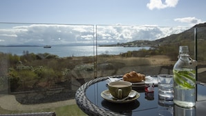 A table with a croissant, a cup of coffee, and a water bottle, overlooking a scenic view of a lake and mountains. - The Isle of Mull Hotel and Spa (Isle of Mull)