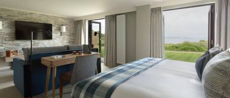 Habitación de hotel con una cama grande, un escritorio con silla, un televisor de pantalla plana en una pared de piedra y vistas al exterior.