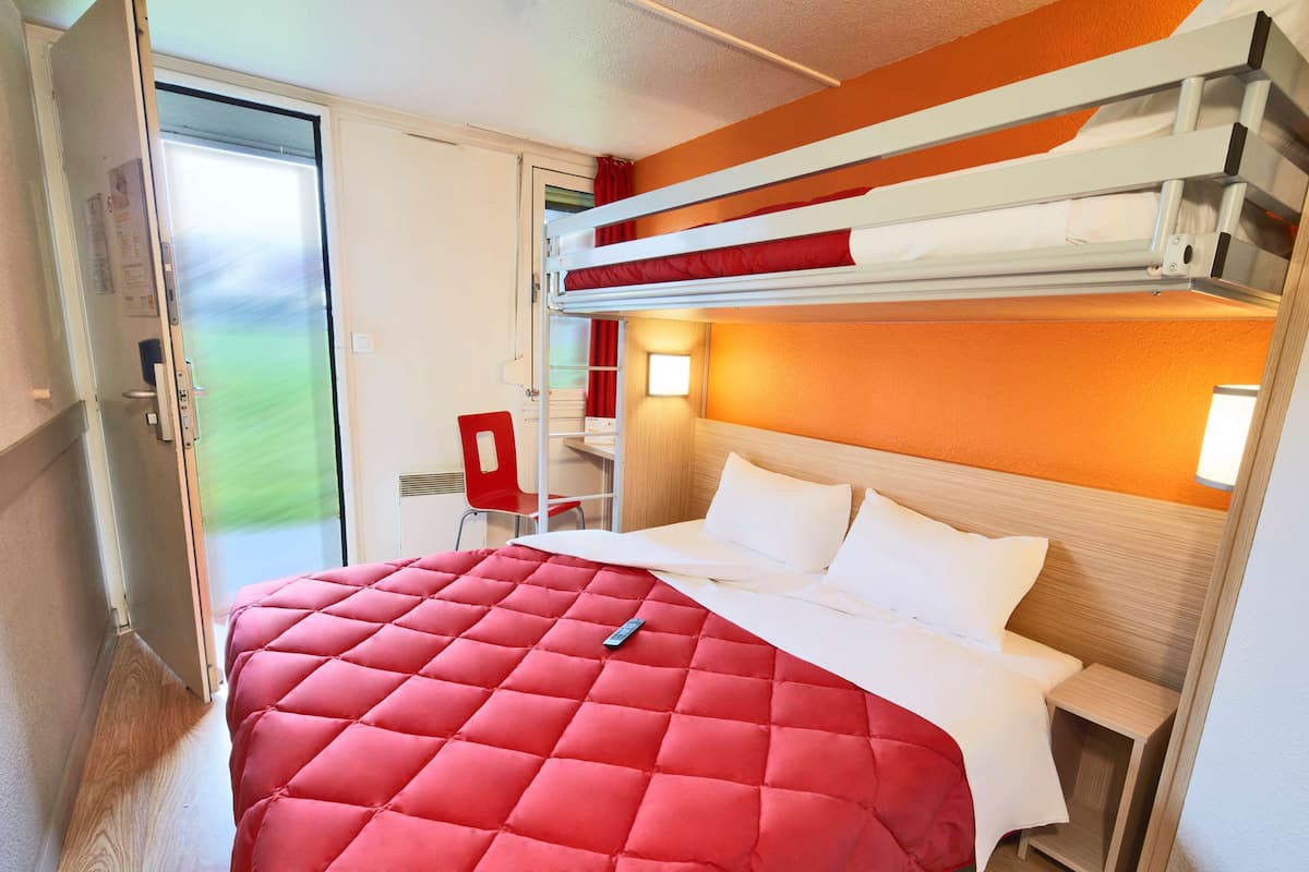 Une chambre avec un lit superposé, une couette rouge matelassée, une tête de lit en bois, une table de chevet et une chaise rouge.