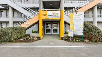 A hotel entrance with a yellow and white color scheme, multiple floors, and a staircase leading to the entrance.