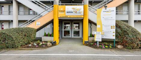 A hotel entrance with a yellow and white color scheme, multiple floors, and a staircase leading to the entrance.