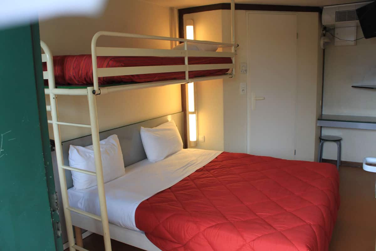 Ein Stockbett mit einer roten Steppdecke, einem weißen Kopfkissen und einer weißen Decke.