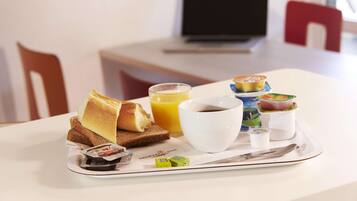 A breakfast tray with toast, juice, coffee, yogurt, and a newspaper on a hotel table.