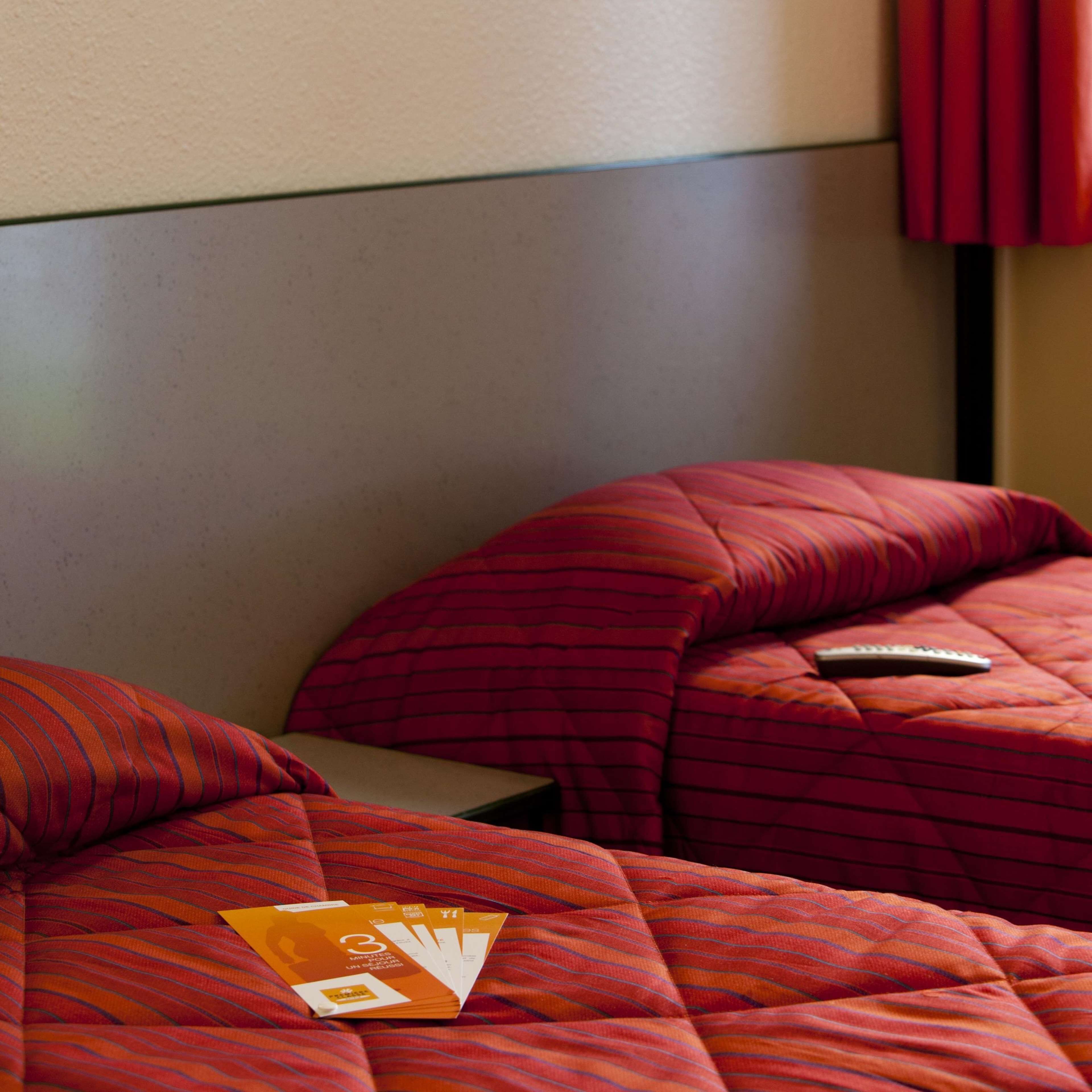 Habitación de hotel con dos camas, cada una con ropa de cama roja y un control remoto sobre una de ellas.