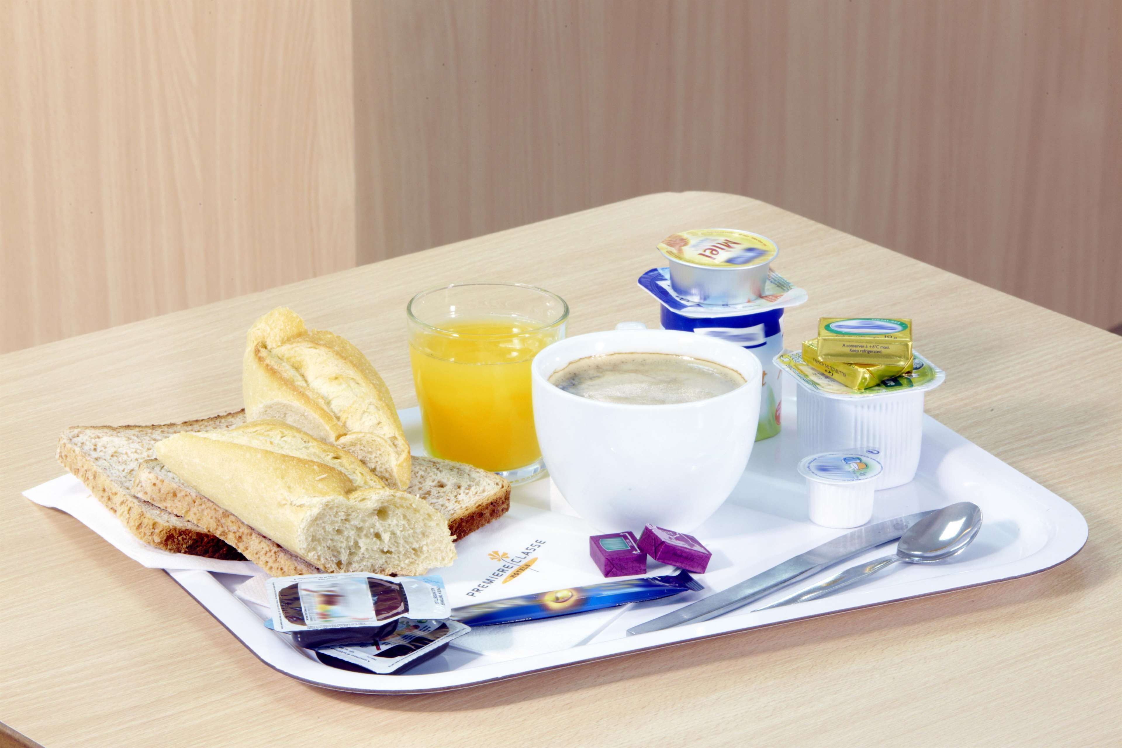 A breakfast tray with toast, orange juice, coffee, butter, jam, and a newspaper.