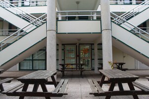 Entrada de un edificio con dos escaleras, un letrero que dice 'PREMIERE CLASSE' y tres mesas de picnic de madera.
