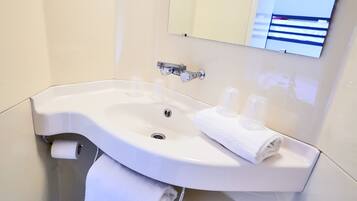 A white bathroom sink with a mirror above it, a towel rack, and a toilet paper holder.