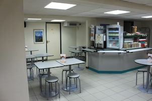 Una cafetería con mesas, sillas altas y un refrigerador, además de un mostrador con distintos productos.