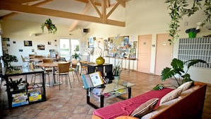 A spacious living area with a sofa, coffee table, and dining table. There are several chairs, a hanging plant, and a bulletin board with various papers and pictures. - Résidence Soko-Eder (Ciboure)
