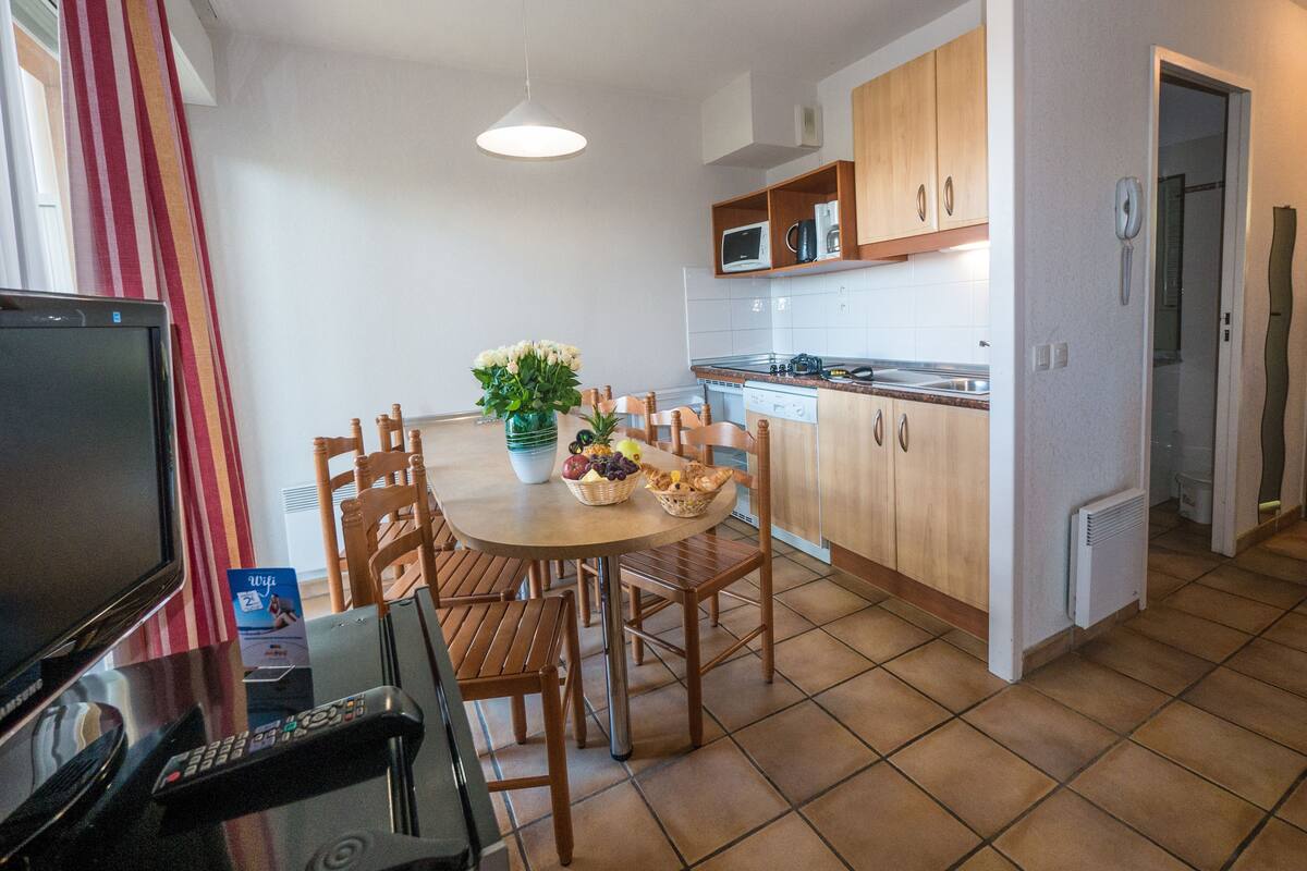 Eine moderne Küche mit Holzschränken, einem Esstisch mit Stühlen, einem Fernseher und einer Fernbedienung auf dem Tisch.