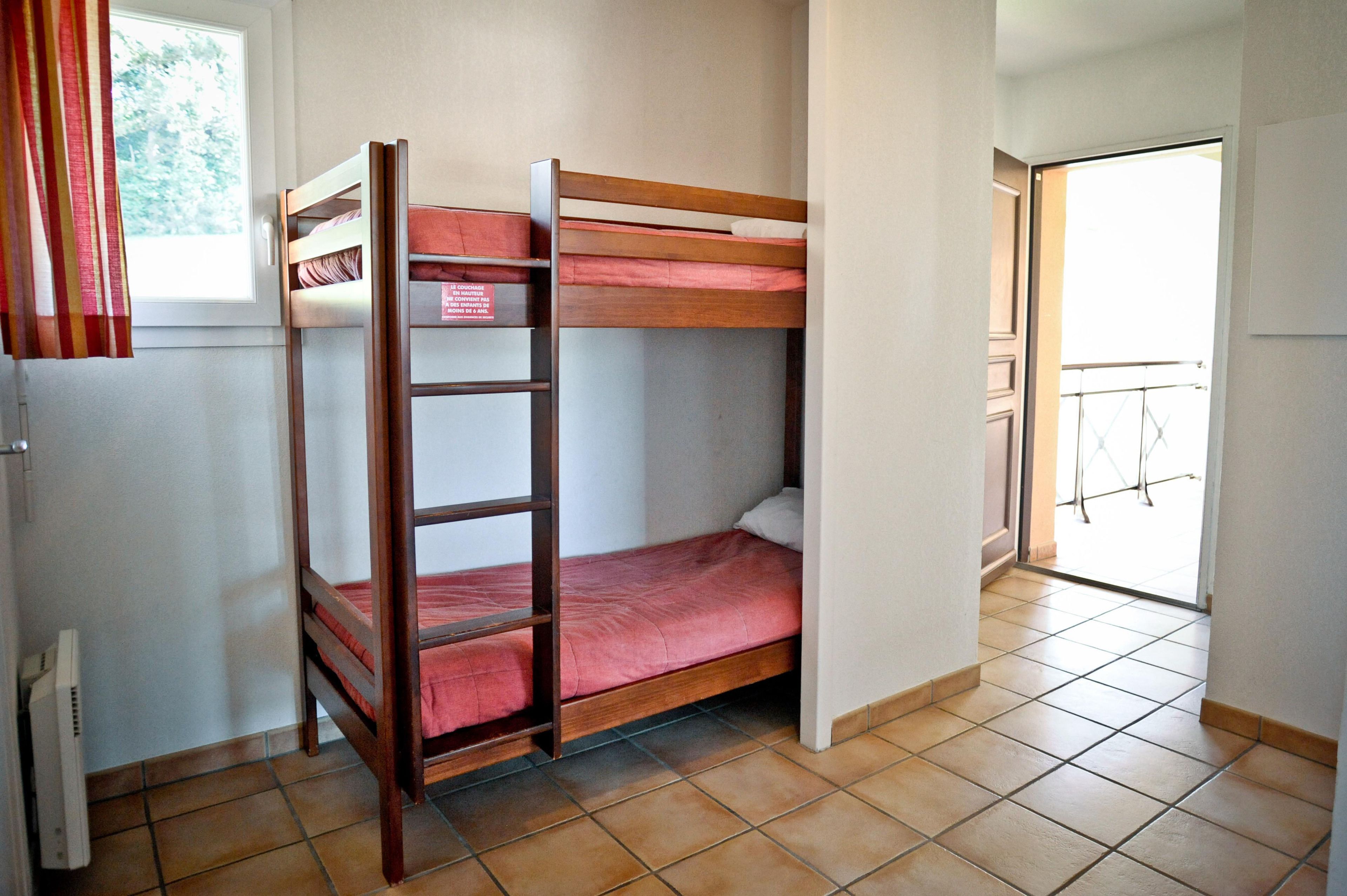 A bunk bed room with a ladder, a window with curtains, and a door leading to a balcony.