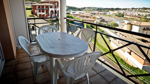 A balcony with a table and chairs, overlooking a residential area with houses and a river. - Résidence Soko-Eder (Ciboure)