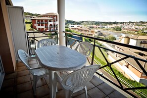 Un balcon avec une table et des chaises, donnant sur un quartier résidentiel avec des maisons et une rivière.