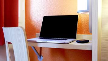 Un espacio de trabajo con una computadora portátil sobre un escritorio, una silla y un monitor.