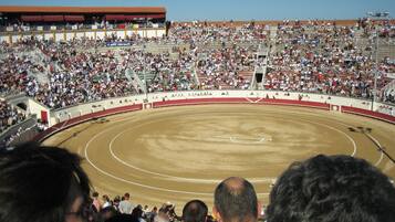 A bullfighting arena with a circular ring, tiered seating, and a crowd of spectators.