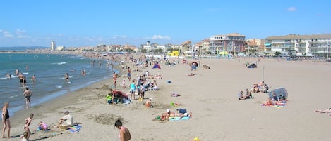 A crowded beach with people sunbathing and swimming.