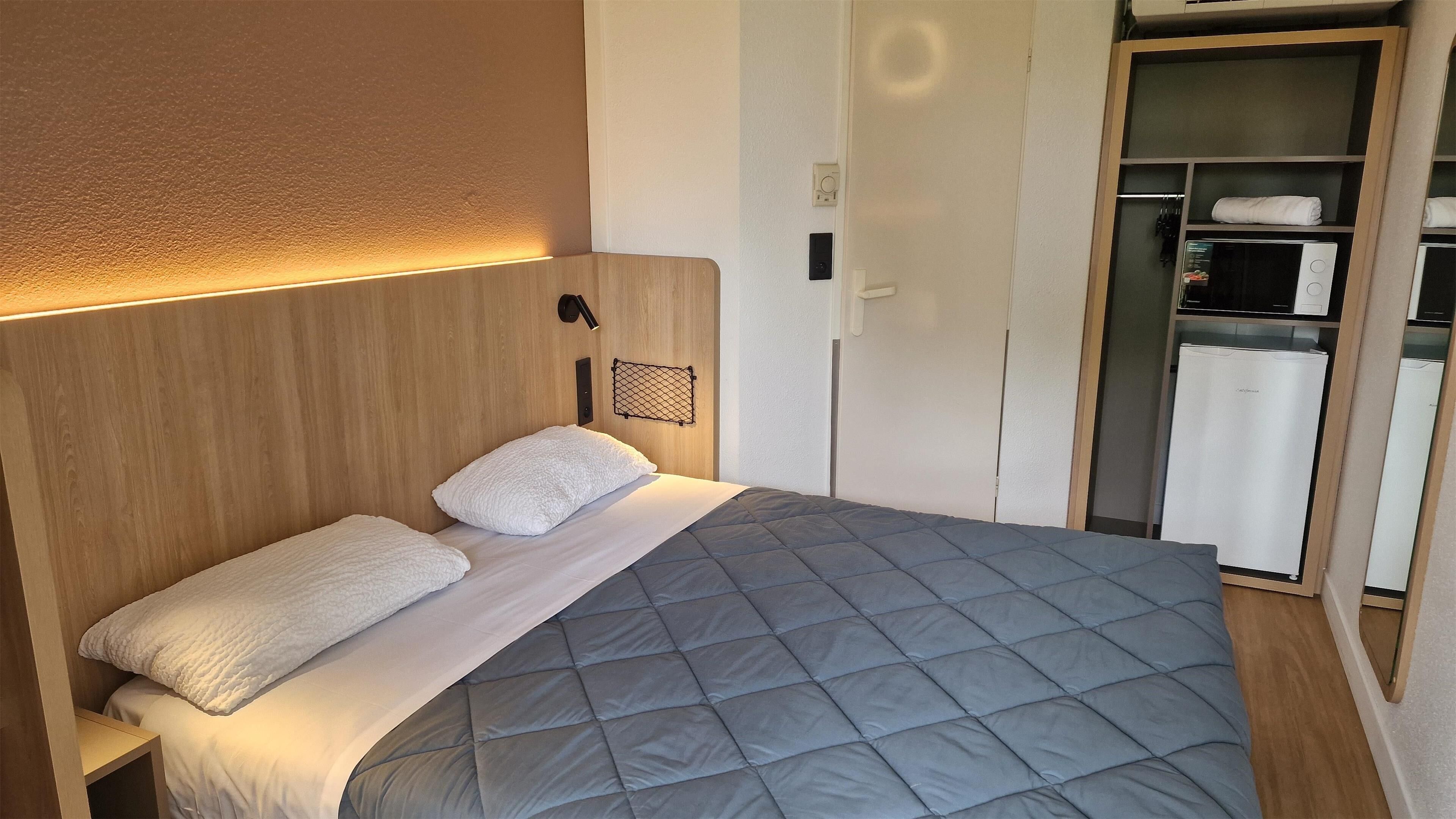 Una cama bien tendida con un edredón gris, almohadas blancas y un cabecero de madera.