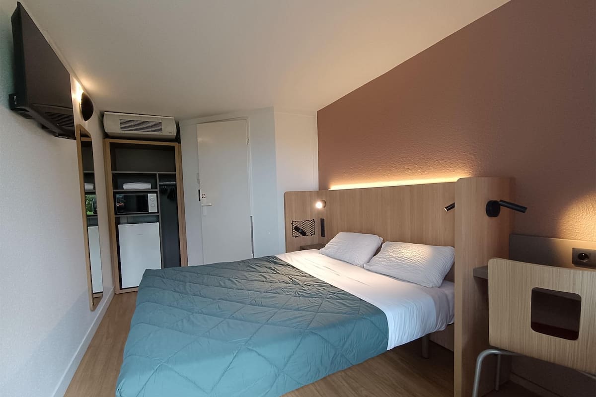 A hotel room with a bed, a desk, a chair, a wardrobe, and a TV.
