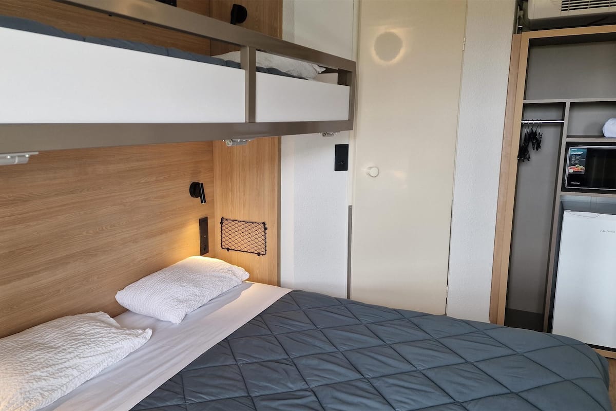 A bunk bed with a wooden headboard, a small shelf, and a wall-mounted light.