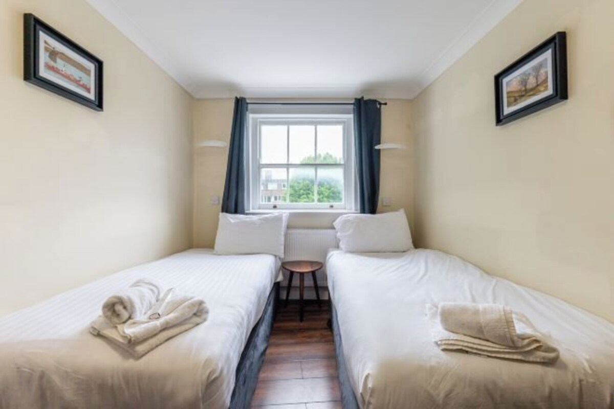 A room with two beds, a small table, and a window with curtains.
