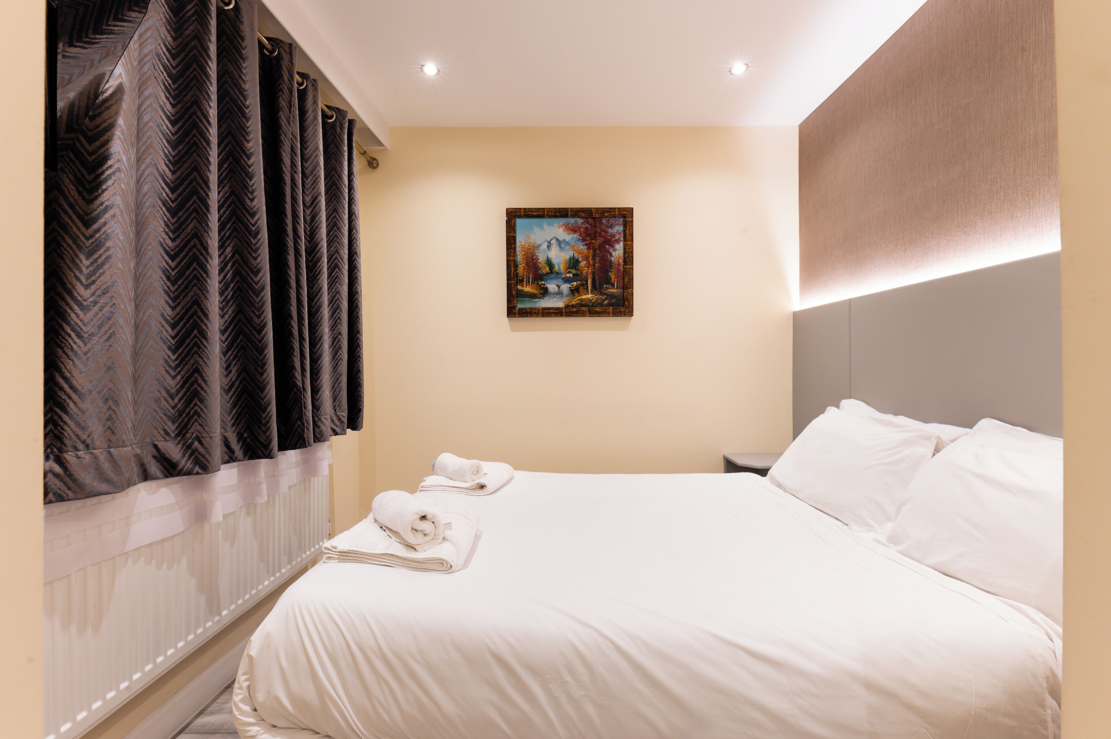 Una habitació d'hotel amb un llit ben fet, un quadre a la paret i una finestra amb cortines.