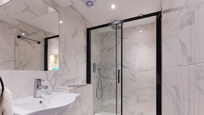 A modern bathroom with a marble-tiled shower enclosure, a white sink, and a toilet. - Belmont Hotel (London)