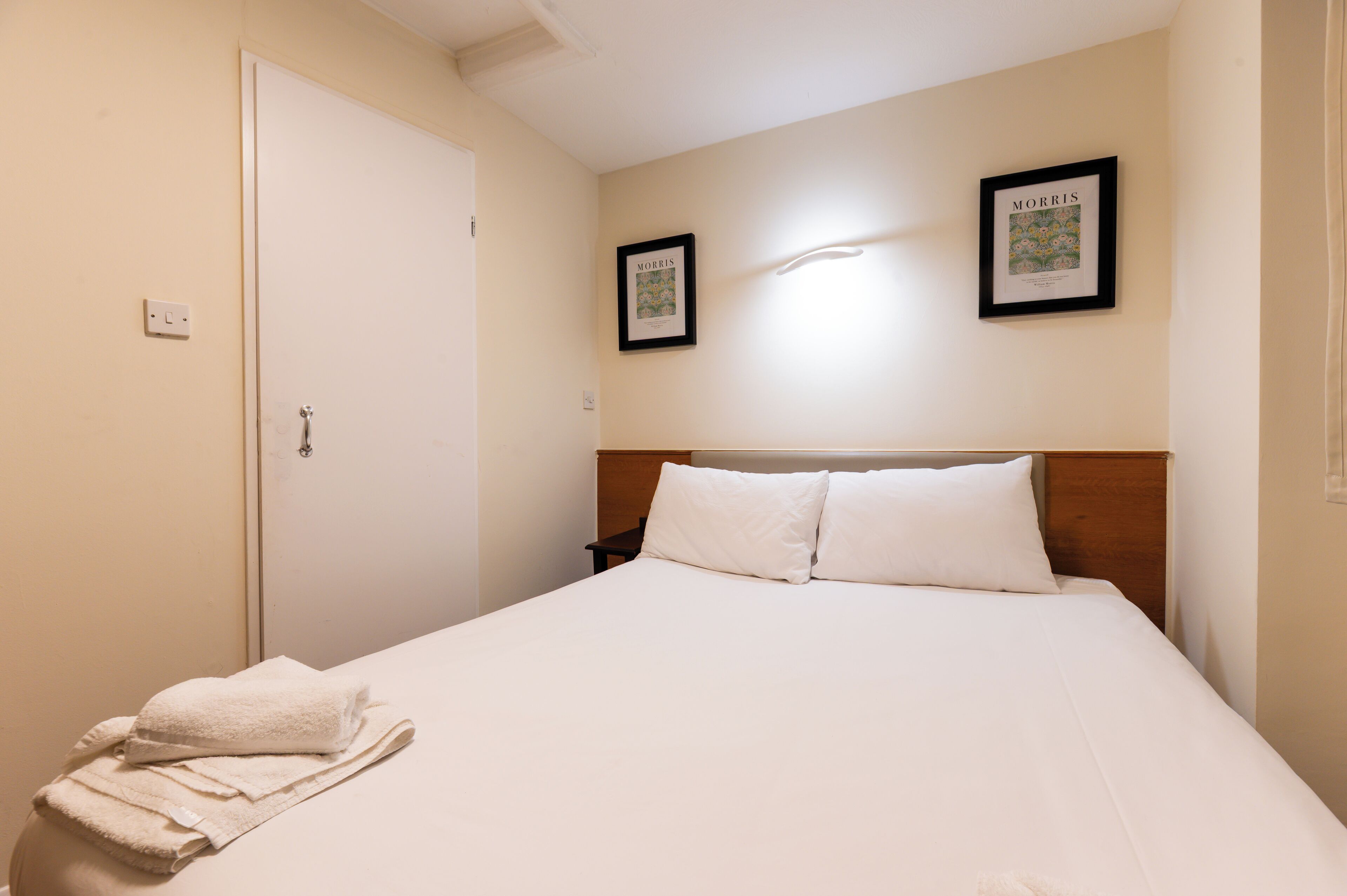 A hotel room with a bed, two framed pictures on the wall, a door, and a towel on the floor.