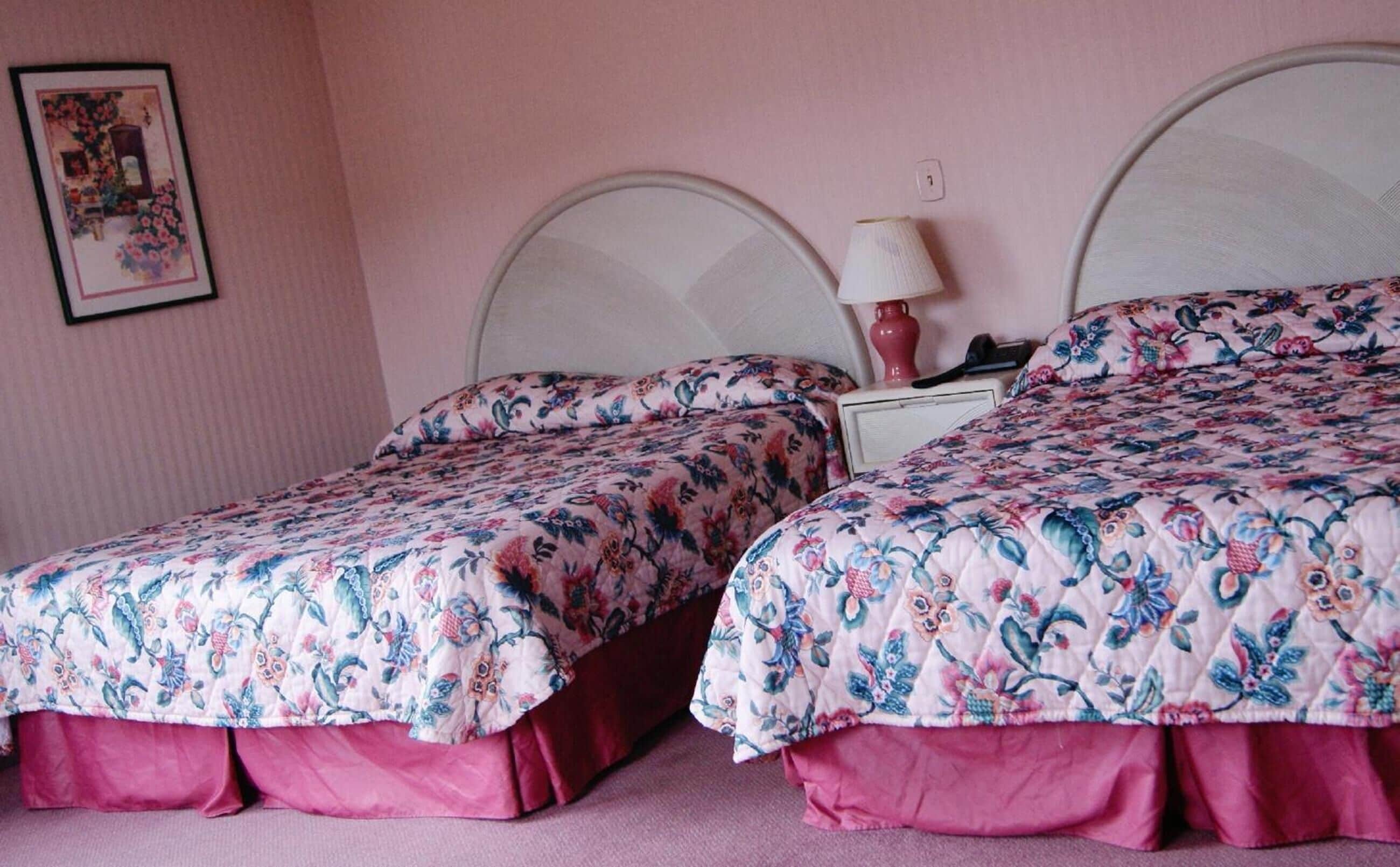 Two beds with floral bedding, a bedside table with a lamp, and a framed picture on the wall.