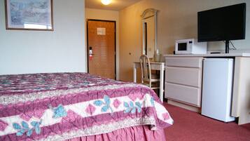 A hotel room with a bed, a desk with a chair, a microwave, a television, and a refrigerator.