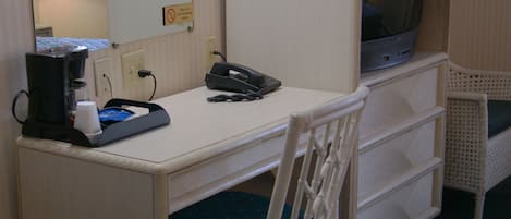 A compact hotel room with a single bed, a small desk with a telephone, a coffee maker, and a television.