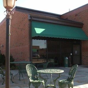 A brick building with a green awning, outdoor seating with metal chairs and a table, and a street lamp.