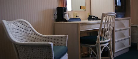 A room with a wicker chair, a desk with a computer, a coffee maker, and a television.